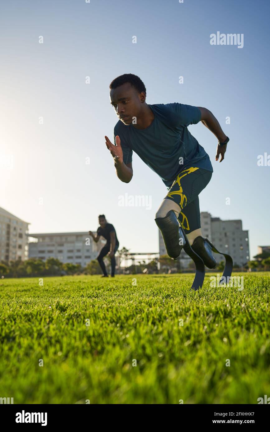 Fokussiertes Sprintertraining mit männlichen Amputierten auf einem sonnigen Sportplatz Stockfoto