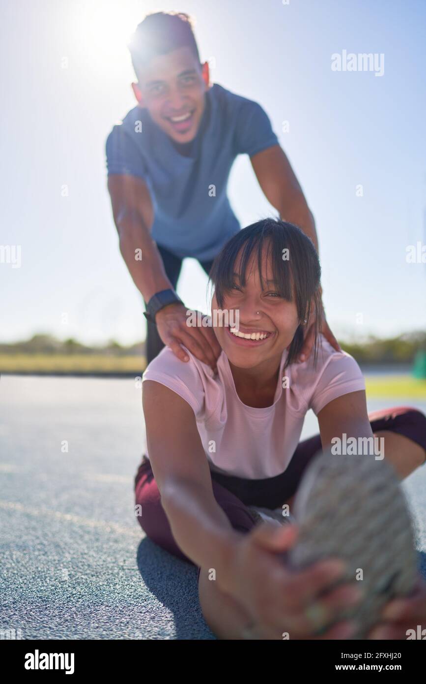 Porträtieren Sie glückliche, selbstbewusste junge Läufer, die sich auf der sonnigen Sportstrecke strecken Stockfoto