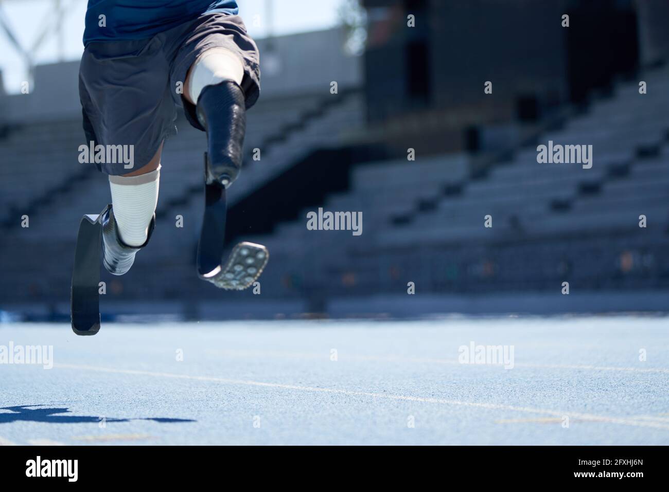 Amputierte männliche Sportlerin, die auf einer sonnigen blauen Sportstrecke sprintet Stockfoto