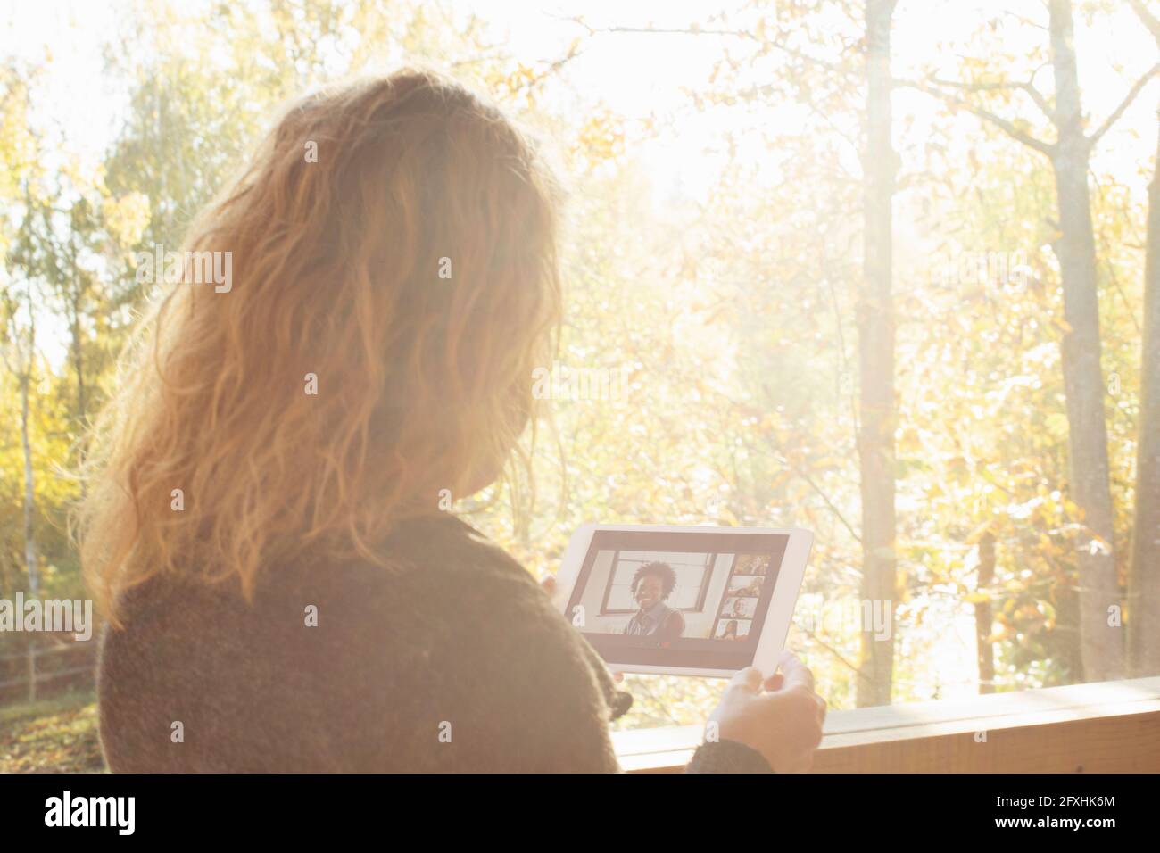 Frau chattet mit Freunden auf einem digitalen Tablet am sonnigen Fenster Stockfoto