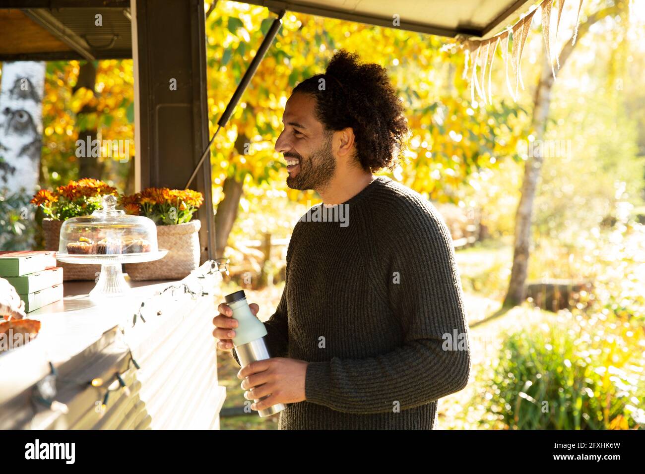 Lächelnder männlicher Kunde, der im Herbstpark vom Food Truck bestellt Stockfoto