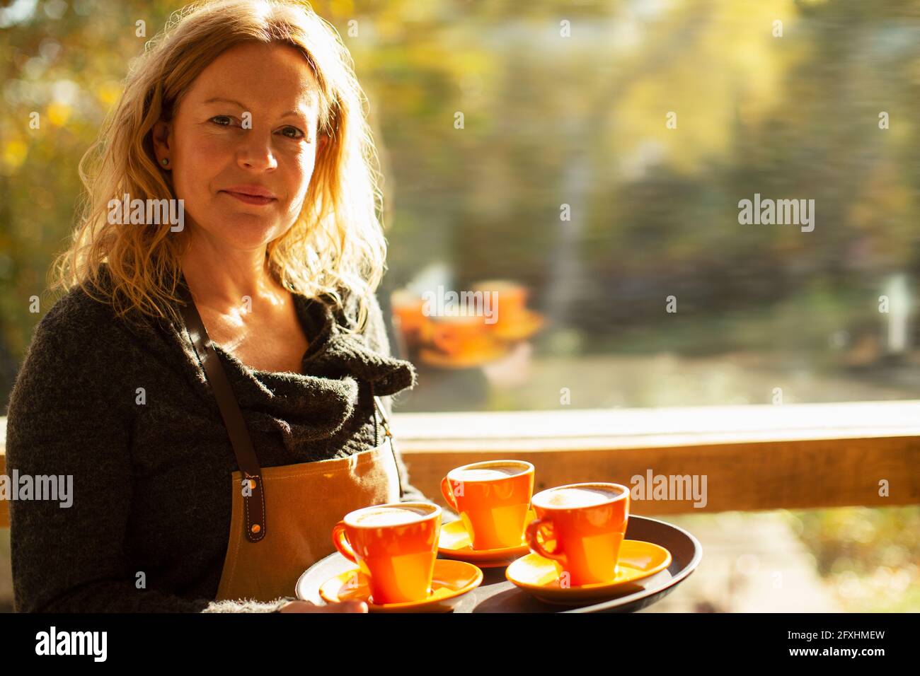 Eine selbstbewusste Barista mit einem Tablett mit Kaffee im sonnigen Fenster Stockfoto