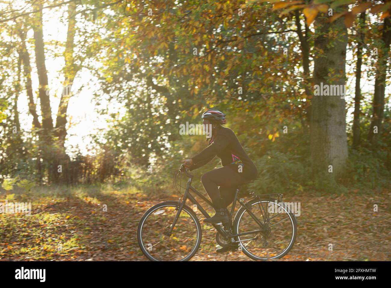 Glückliche Frau Fahrrad fahren zwischen Herbstblättern im sonnigen Park Stockfoto