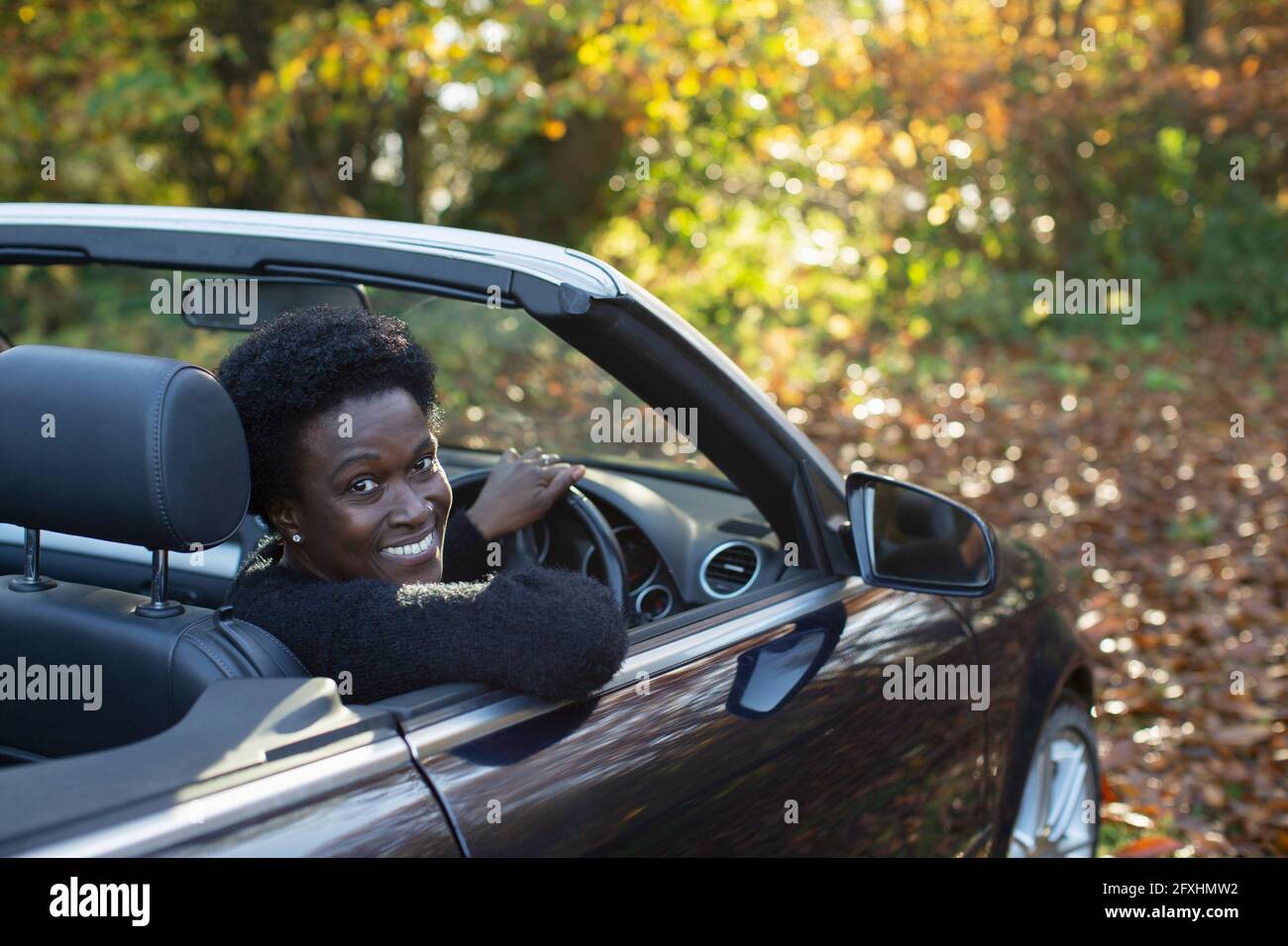 Portrait glückliche Frau fährt Cabrio im Herbstpark Stockfoto