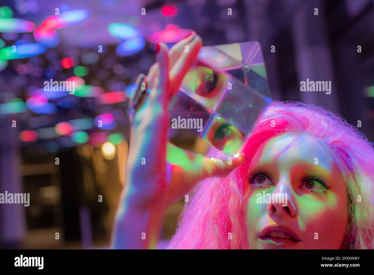 Frau mit rosafarbenem Haar, die zu einem dimensionalen Kristallwürfel aufschaut Stockfoto