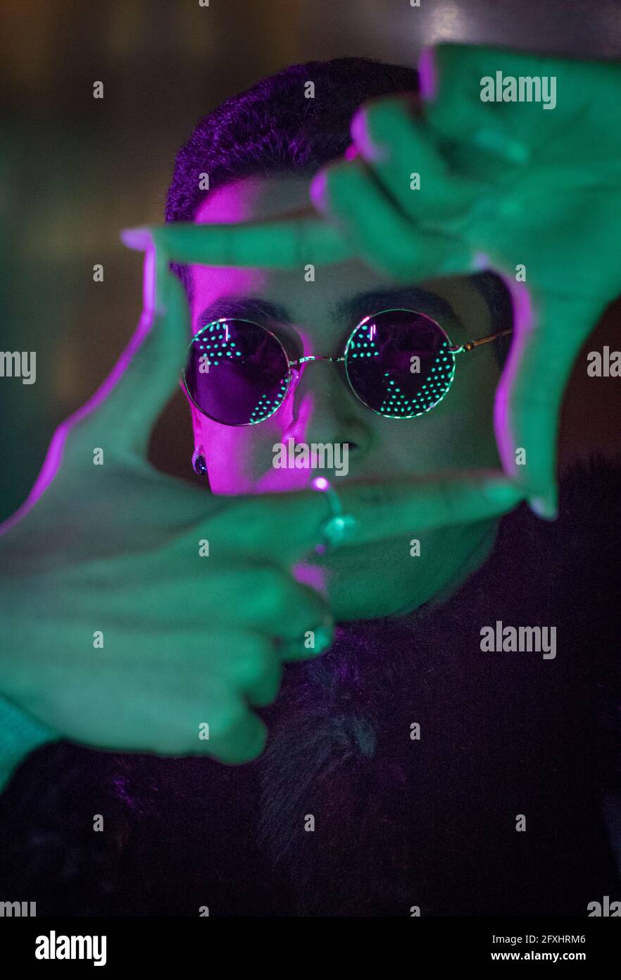 Portrait coole junge Mann in Sonnenbrille bilden Fingerrahmen in Neon Stockfoto