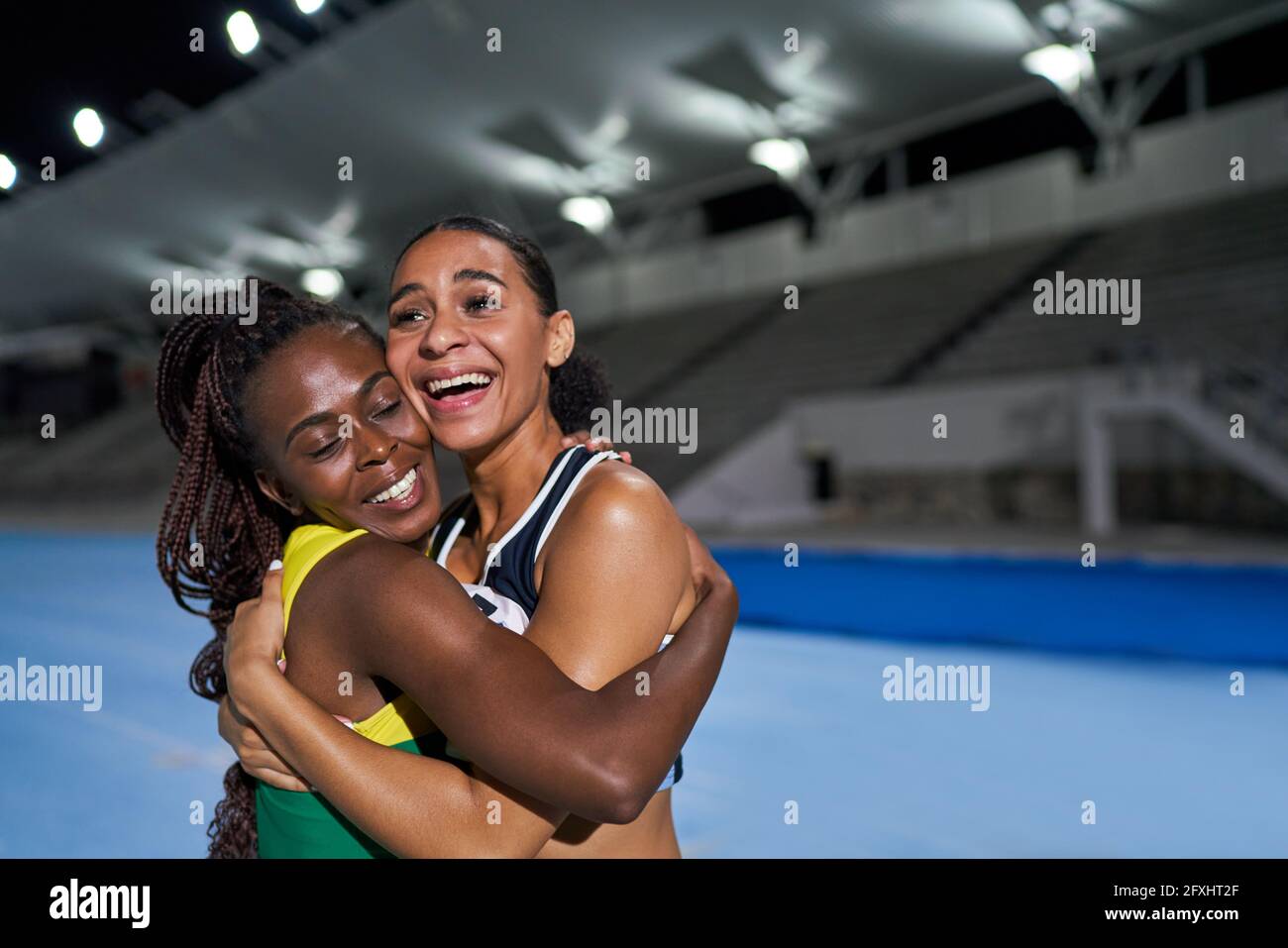 Glückliche weibliche Leichtathleten umarmen sich nachts auf der Strecke Stockfoto
