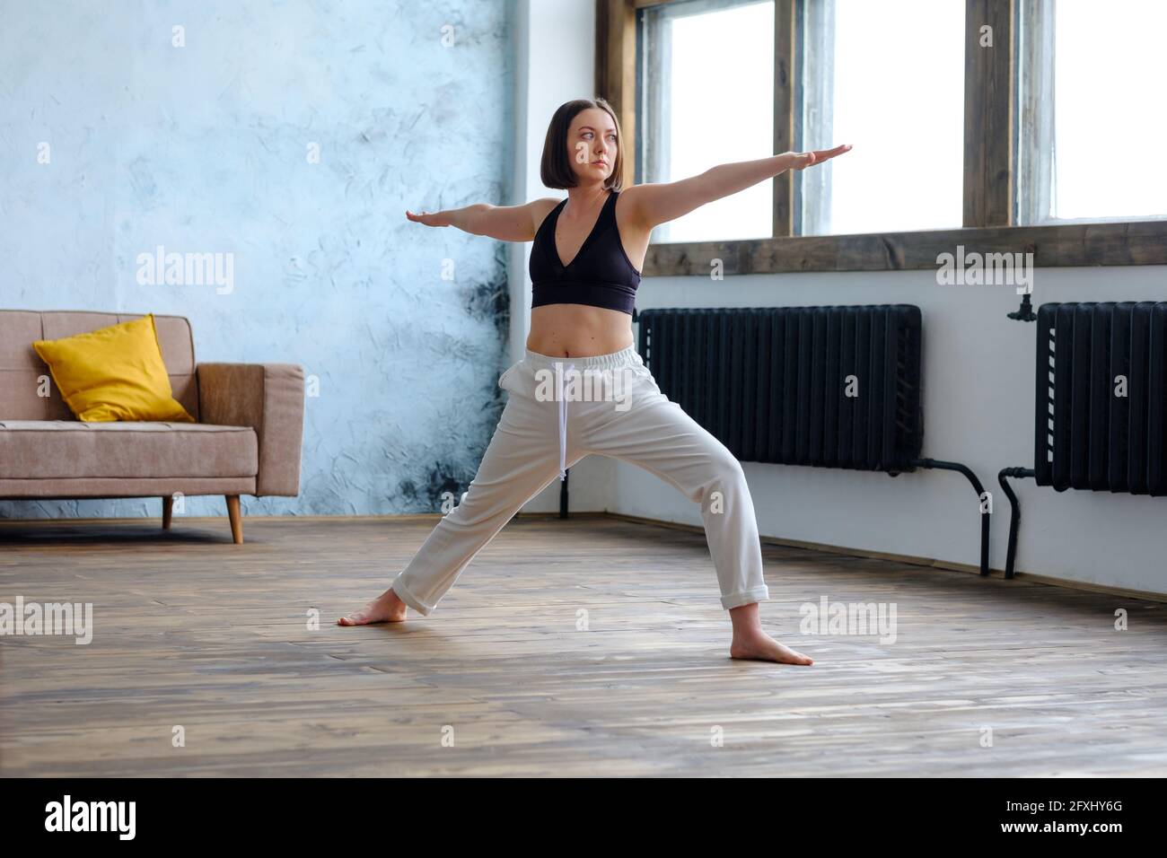 Frau in ihrem Wohnzimmer in Krieger-Yoga-Pose. Stockfoto
