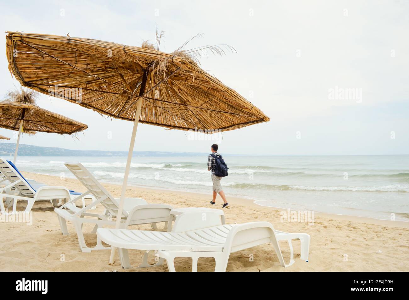 Leerer Strand mit einsamen Reisenden mit Rucksack, der gegen den läuft Hintergrund des Meeres Stockfoto