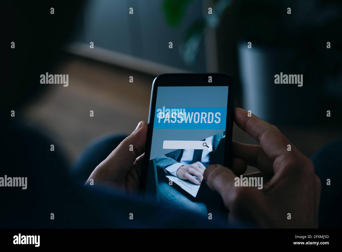 Ein junger Kaukasusmann verwendet zu Hause einen Passwort-Manager in seinem Smartphone, auf dem eine simulierte Passwort-Manager-App auf dem Bildschirm angezeigt wird Stockfoto