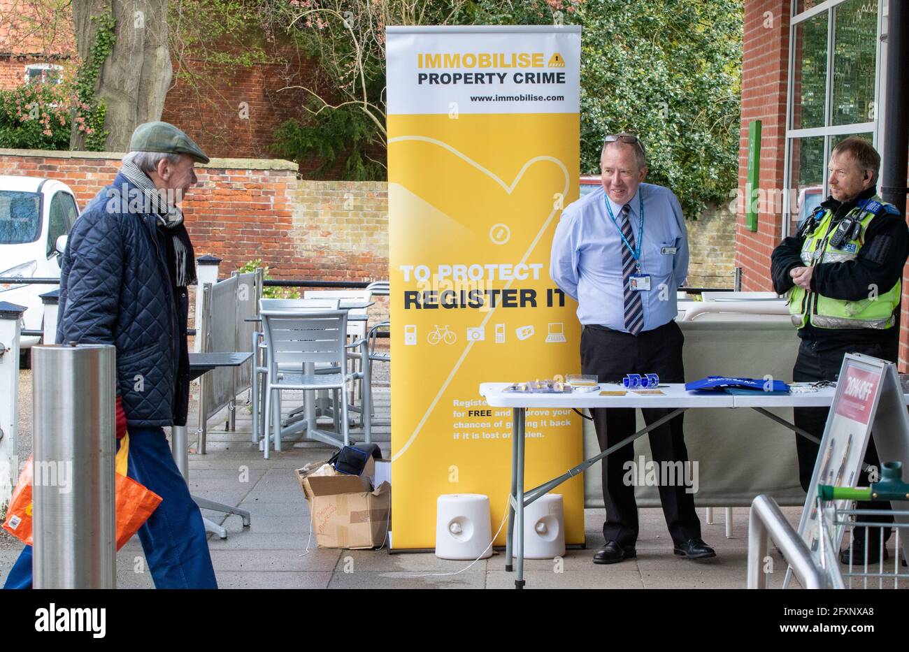 Der Community Police Support Officer und der Civilian Crime Prevention Officer sprechen Zu den Käufern an einem Supermarkt Eingang Stockfoto