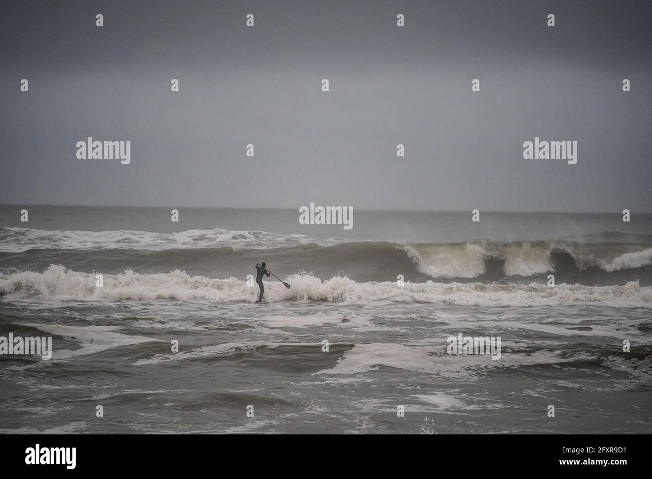 Mann, der versucht, auf seinem Stand-up-Paddle-Board, Nags Head, North Carolina, Vereinigte Staaten von Amerika, Nordamerika, durch einen großen Küstenbruch zu kommen Stockfoto