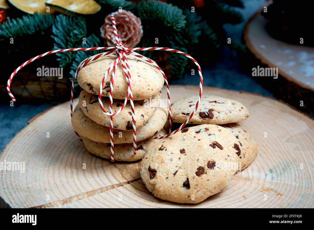 Haferflockenkuchen mit Schokoladenstücken. Ein Stapel von Lebern, die mit einer rot-weißen Kordel vor dem Hintergrund eines Weihnachtsbaums gebunden sind Stockfoto