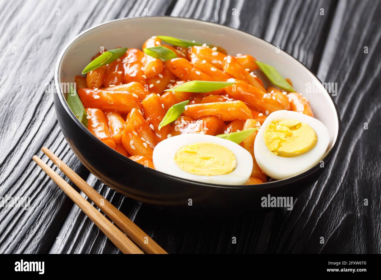 Tteokbokki dukbokki ist ein beliebtes koreanisches Street Food, das aus weichen, zähigen Reiskuchen hergestellt wird, die in einer süßen und würzigen Sauce in einer Schüssel auf dem Tisch in der Nähe zubereitet werden. Stockfoto