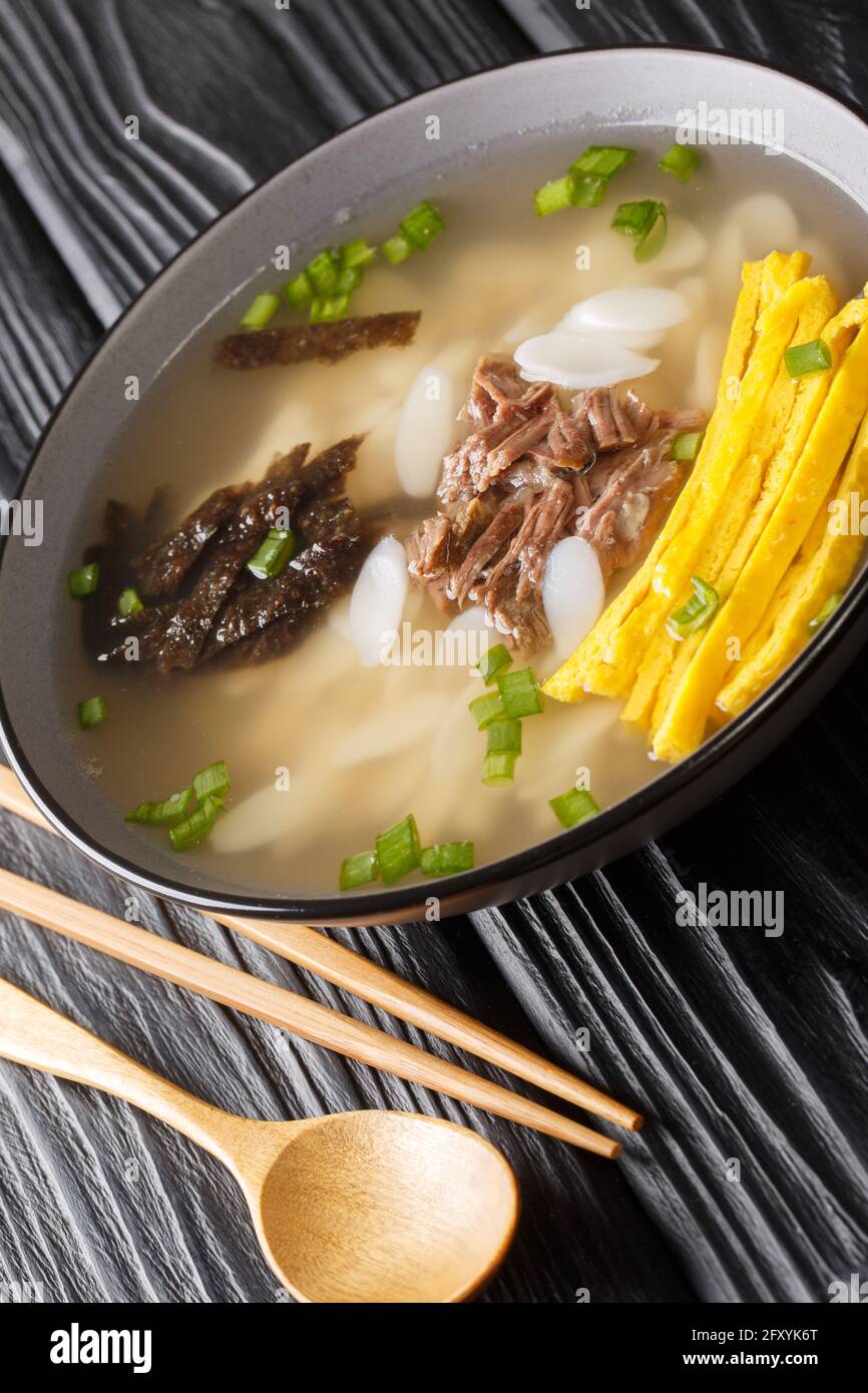 Herzhafte und beruhigende koreanische Reiskuchen-Suppe Tteokguk in der Schüssel auf dem Tisch. Vertikal Stockfoto