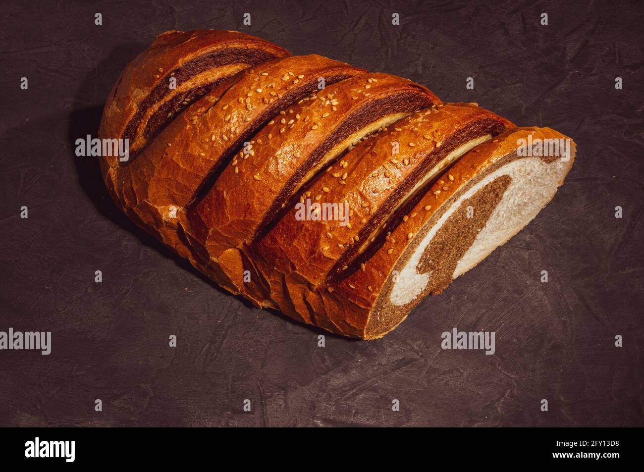 Ungewöhnlicher zweifarbiger frischer Laib Brot auf schwarzem Hintergrund, Foto in einer niedrigen Taste bei hartem Licht, Nahaufnahme Stockfoto