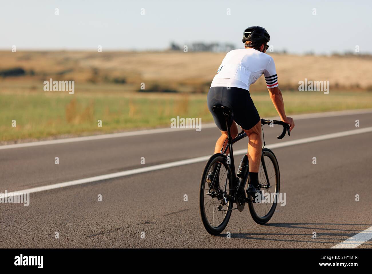 Rückansicht des Radfahrers im Helm Radfahren auf Asphaltstraße Stockfoto