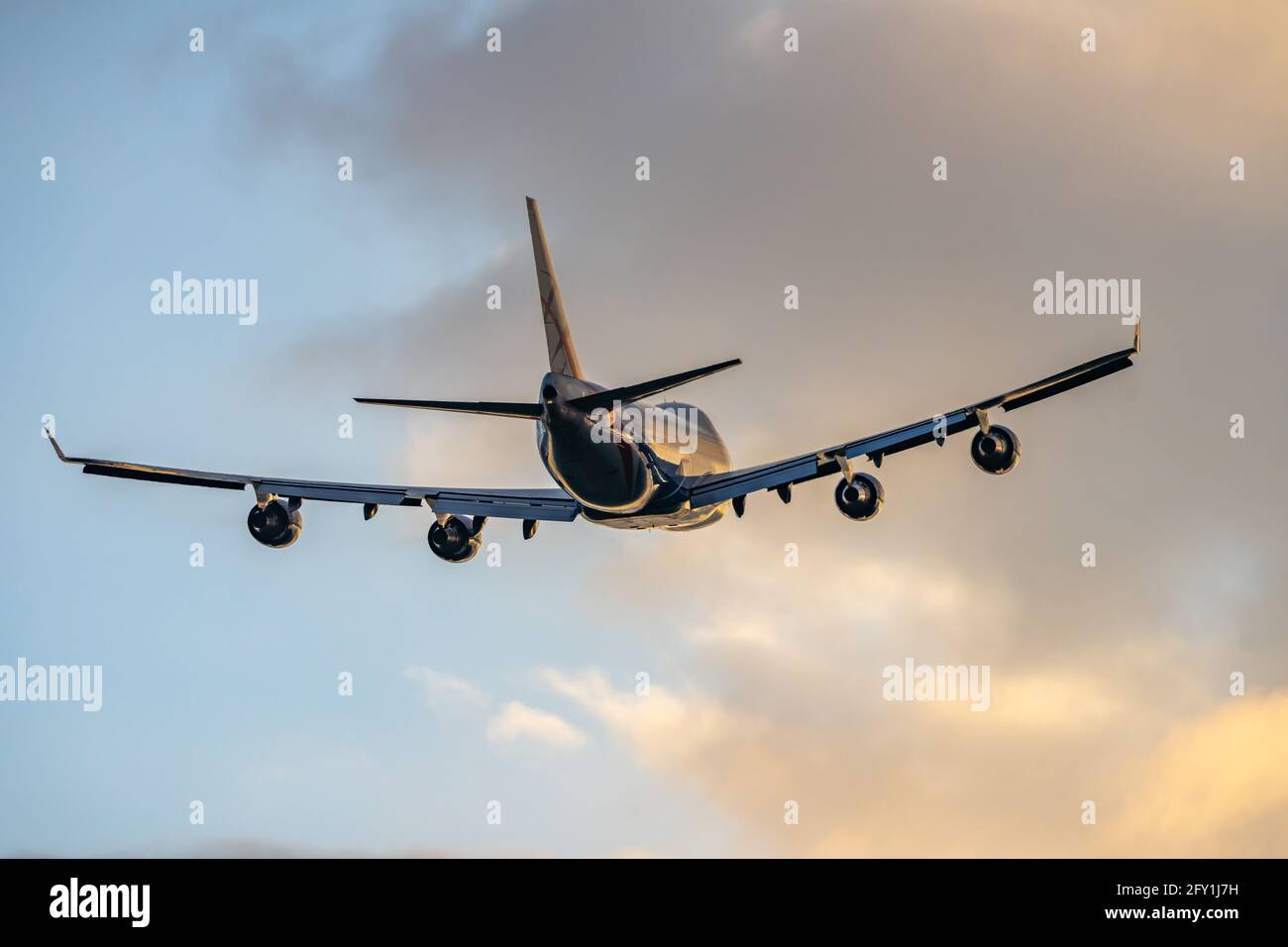 Jumbo Jet vier große Triebwerke fliegen ab und bringen Touristen im Ausland vom Flughafen in den Urlaub in den goldenen Sommerhimmel bei Sonnenuntergang. Cremefarbene Goldwolken und Silhouette Stockfoto