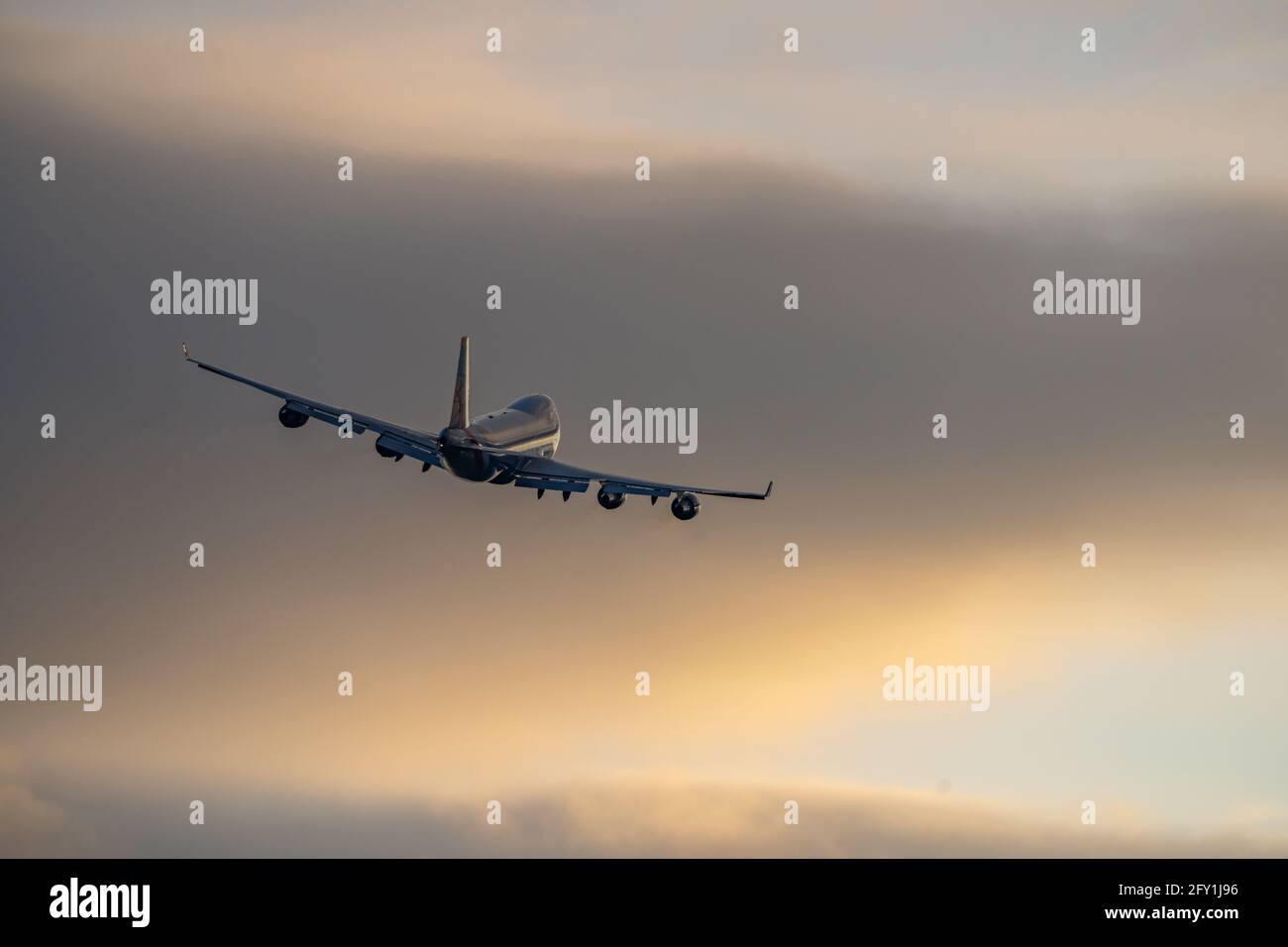 Jumbo Jet vier große Triebwerke fliegen ab und bringen Touristen im Ausland vom Flughafen in den Urlaub in den goldenen Sommerhimmel bei Sonnenuntergang. Cremefarbene Goldwolken und Silhouette Stockfoto