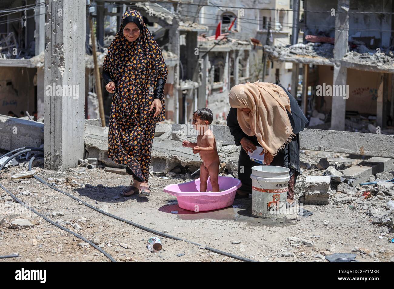 Gaza-Stadt. Mai 2021. Die Mutter des palästinensischen Kindes, Imad Naseer, badet ihr Kind in einem Plastikbehälter auf den Trümmern ihres zerstörten Hauses in Beit Hanoun. Die Bewohner von Beit Hanoun leiden unter dem Mangel an Wasser und Strom in der Region aufgrund der großen Zerstörung, die das Gebiet aufgrund der israelischen Bombardierung im nördlichen Gazastreifen getroffen hat. Kredit: Majority World CIC/Alamy Live Nachrichten Gutschrift: Majority World CIC/Alamy Live Nachrichten Stockfoto