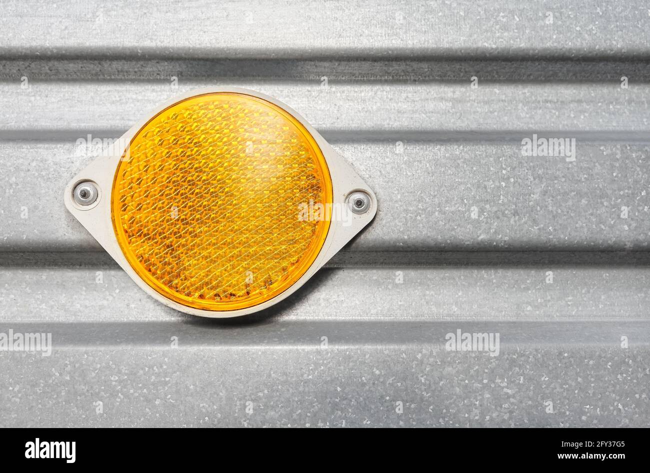 Nahaufnahme eines runden gelben Kunststoffreflektors, der an einer Wellblech-Seite des Anhängers befestigt ist. Stockfoto