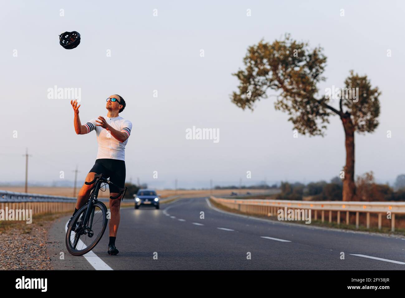 Glücklicher Radfahrer in Sportkleidung wirft schwarzen Helm auf Stockfoto