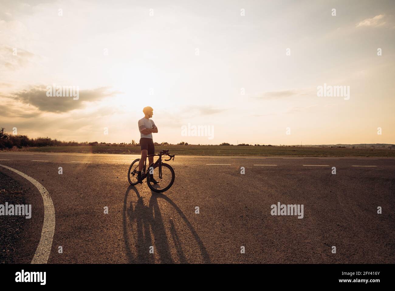 Fröhlicher Radfahrer, der auf der Straße steht und den Sonnenuntergang genießt Stockfoto