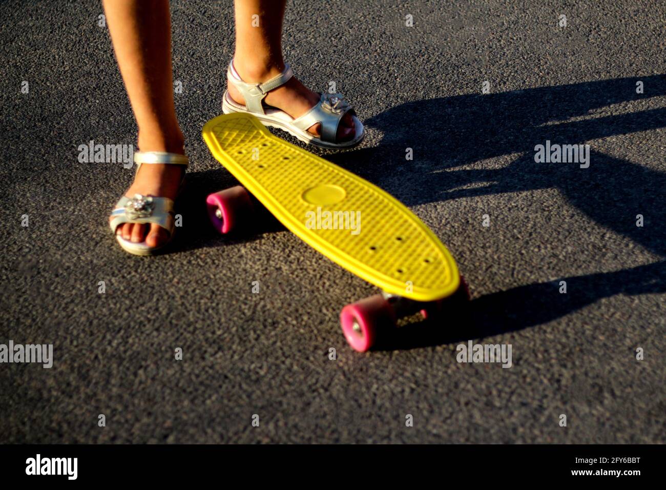 Unschärfe kleine städtische Mädchen stehend mit einem gelben Penny Skateboard. Kleines Kind im Park. City-Stil. Urbane Kinder. Trendy moderne Schatten Hintergrund Stockfoto