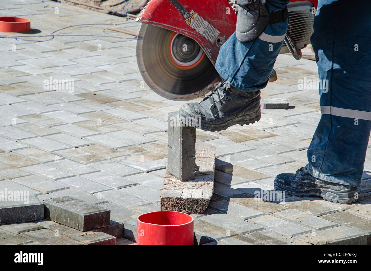 Ein Arbeiter schneidet Pflasterplatten mit einem Gasschneider und Eine Handsäge Stockfoto
