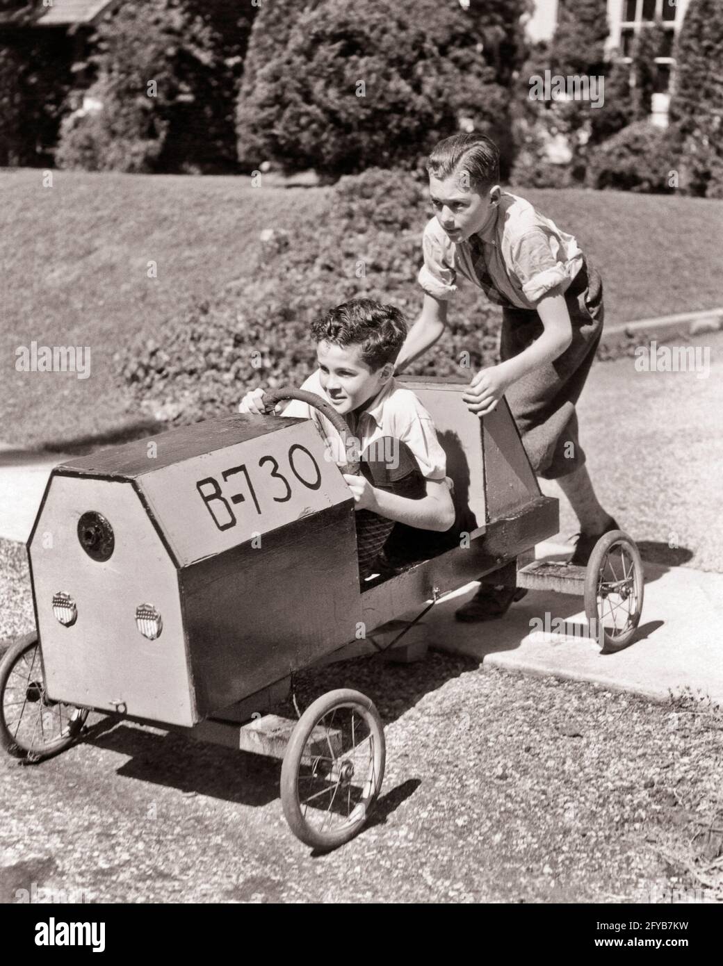 1930ER JAHRE 1940ER JAHRE EIN ERNSTHAFTER JUNGE, DER SEINEN ZWEITEN LÄCHELNDEN JUNGEN SCHOB BRUDER SITZT LENKUNG IHRER HAUSGEMACHTEN SOAP BOX DERBY RENNWAGEN - B16278 HAR001 HARS TEAMWORK WETTBEWERB FREUDE LIFESTYLE GESCHWINDIGKEIT ZUFRIEDENHEIT FEIER BRÜDER HAUS LEBEN KOPIEREN RAUM IN VOLLER LÄNGE INSPIRATION AUTOMOBIL MÄNNER RISIKO GESCHWISTER VERTRAUEN TRANSPORT B&W ERFOLG TRÄUME GLÜCK ABENTEUER DERBY SEINE STÄRKE IHR MUT AUTOS AUFREGUNG KRAFTVOLLEN FORTSCHRITT ERHOLUNG STOLZ GELEGENHEIT GESCHWISTER KONZEPTUELLE AUTOMOBILE ZWEITE STILVOLLE FAHRZEUGE ZUSAMMENARBEIT KREATIVITÄT WACHSTUM HAUSGEMACHTE JUGENDLICHE PRE-TEEN PRE-TEEN JUNGE ENTSPANNUNG Stockfoto