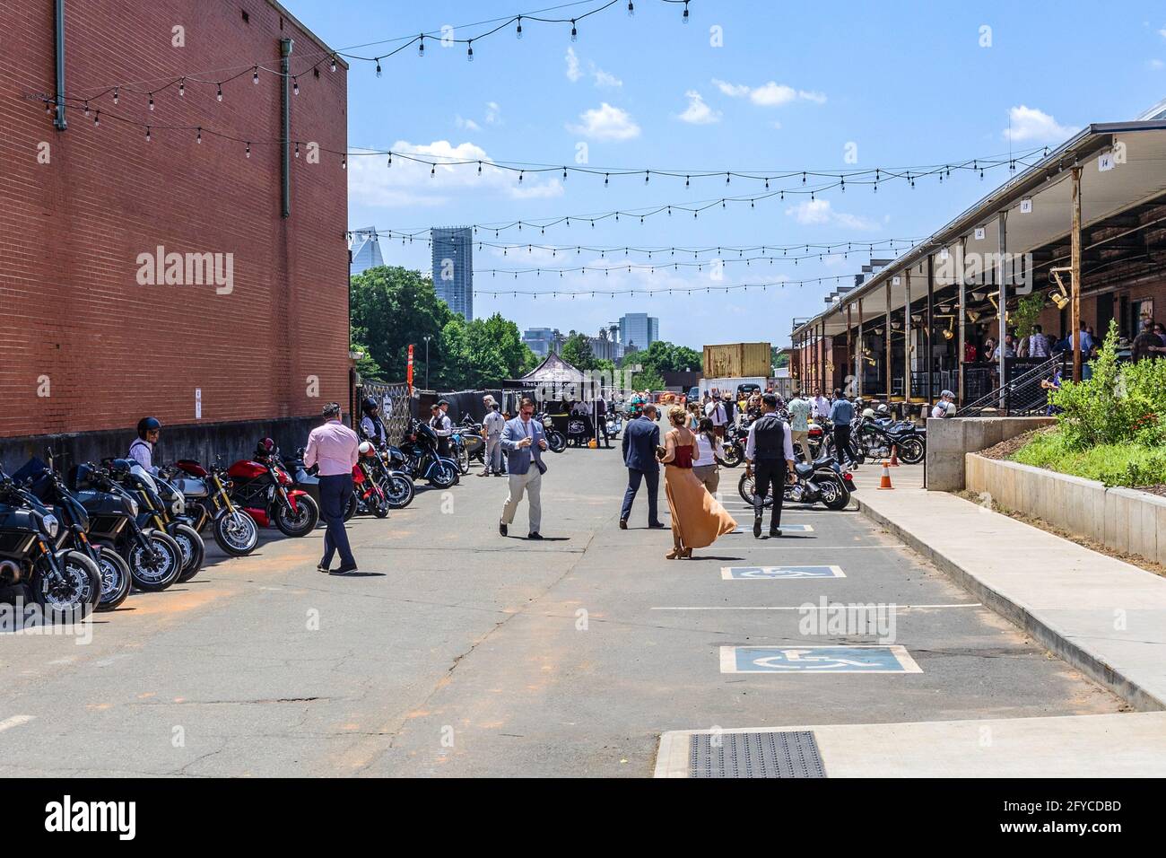 CHARLOTTE, NC, USA-23. MAI 2021: Camp North End. Eine gut gekleidete Menge unter geparkten Motorrädern, die sich mit der Skyline der Stadt in der Ferne unterhalten. Stockfoto