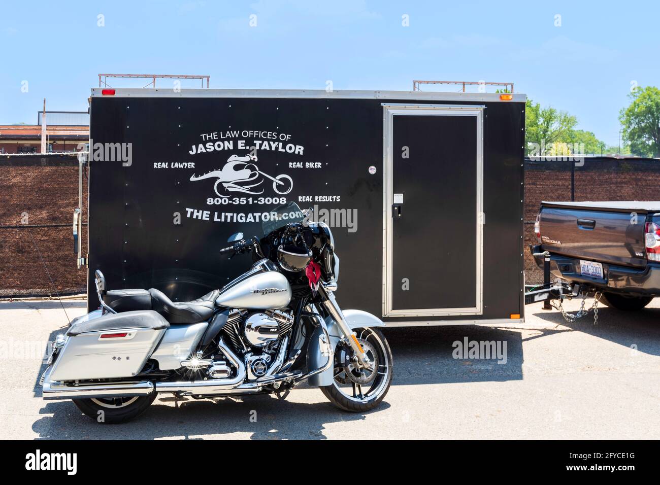 CHARLOTTE, NC, USA-23. MAI 2021: Camp North End. Eine Harley-Davidson Street Glide parkte neben einem Anhänger mit Werbung für einen Unfallanwalt. Stockfoto