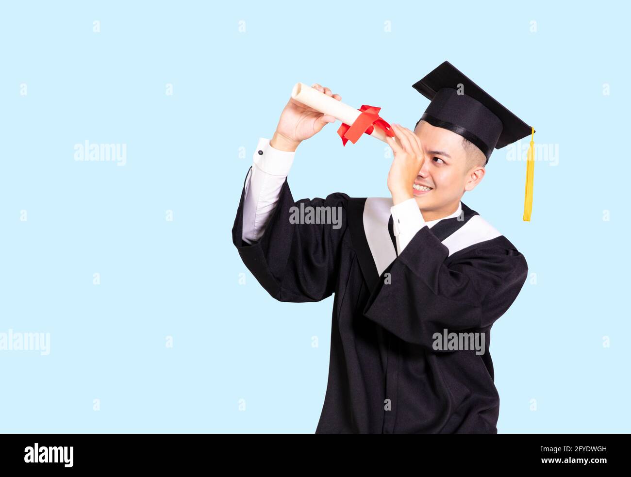 Junge männliche Graduierung halten und durch Diplom schauen Stockfoto