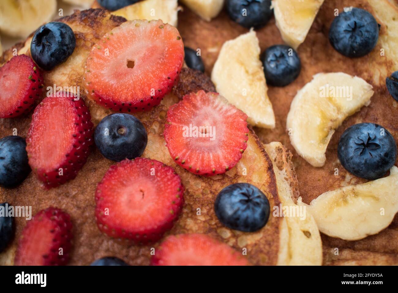 Nahaufnahme von einigen Erdbeeren und Heidelbeeren in Scheiben geschnitten auf zwei Pfannkuchen Auf weißem und hellem Gericht Stockfoto