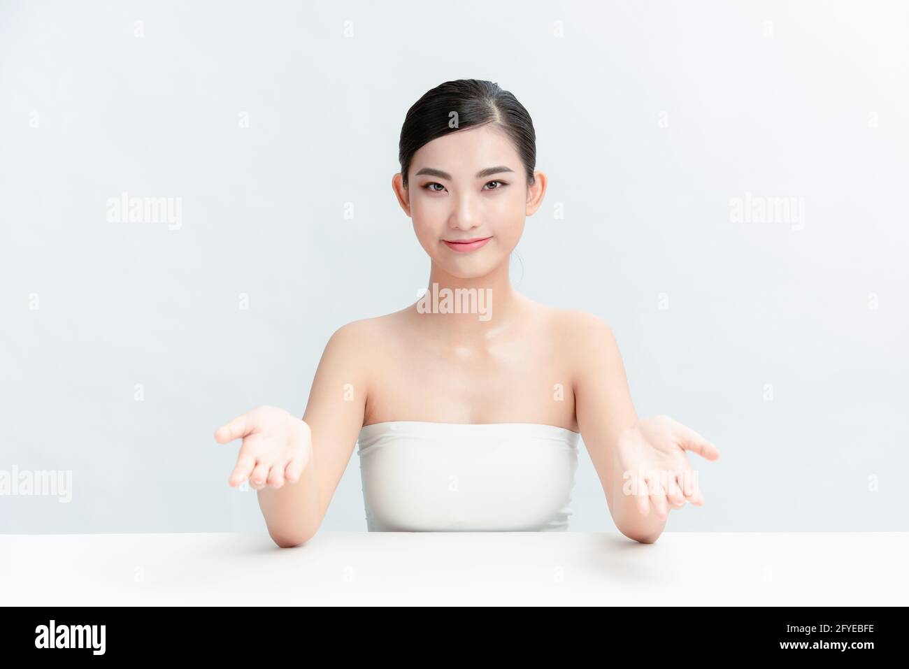 Bestes Produkt. Junge Frau, die vor weißem Hintergrund am Frisiertisch sitzt und Kosmetikprodukte mit einem Lächeln zeigt Stockfoto