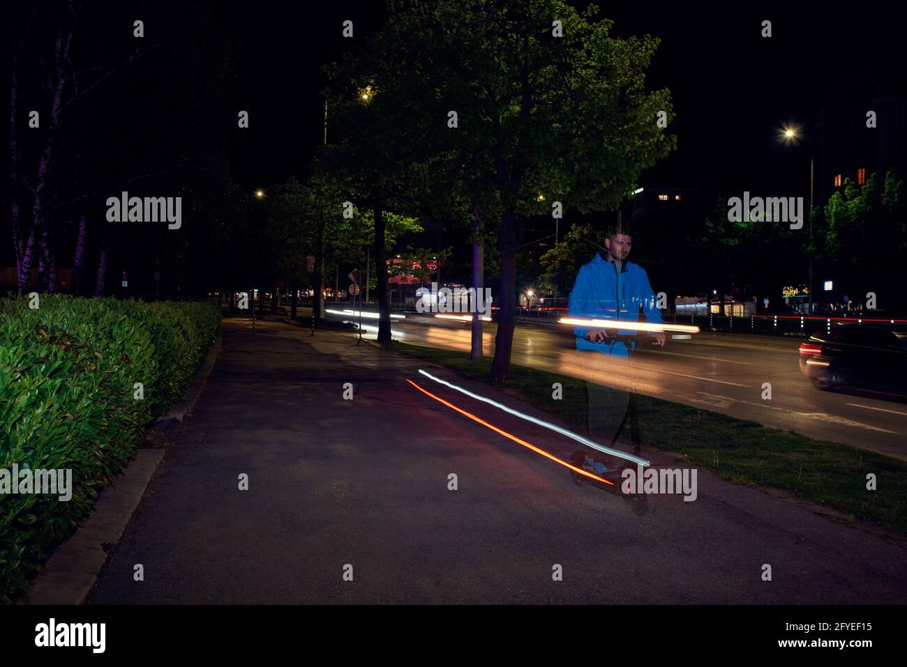 Kaukasischer Mann, der in der Nacht auf der Gasse einen Elektroroller fährt. Verschwommenes Licht und lange Belichtung Stockfoto
