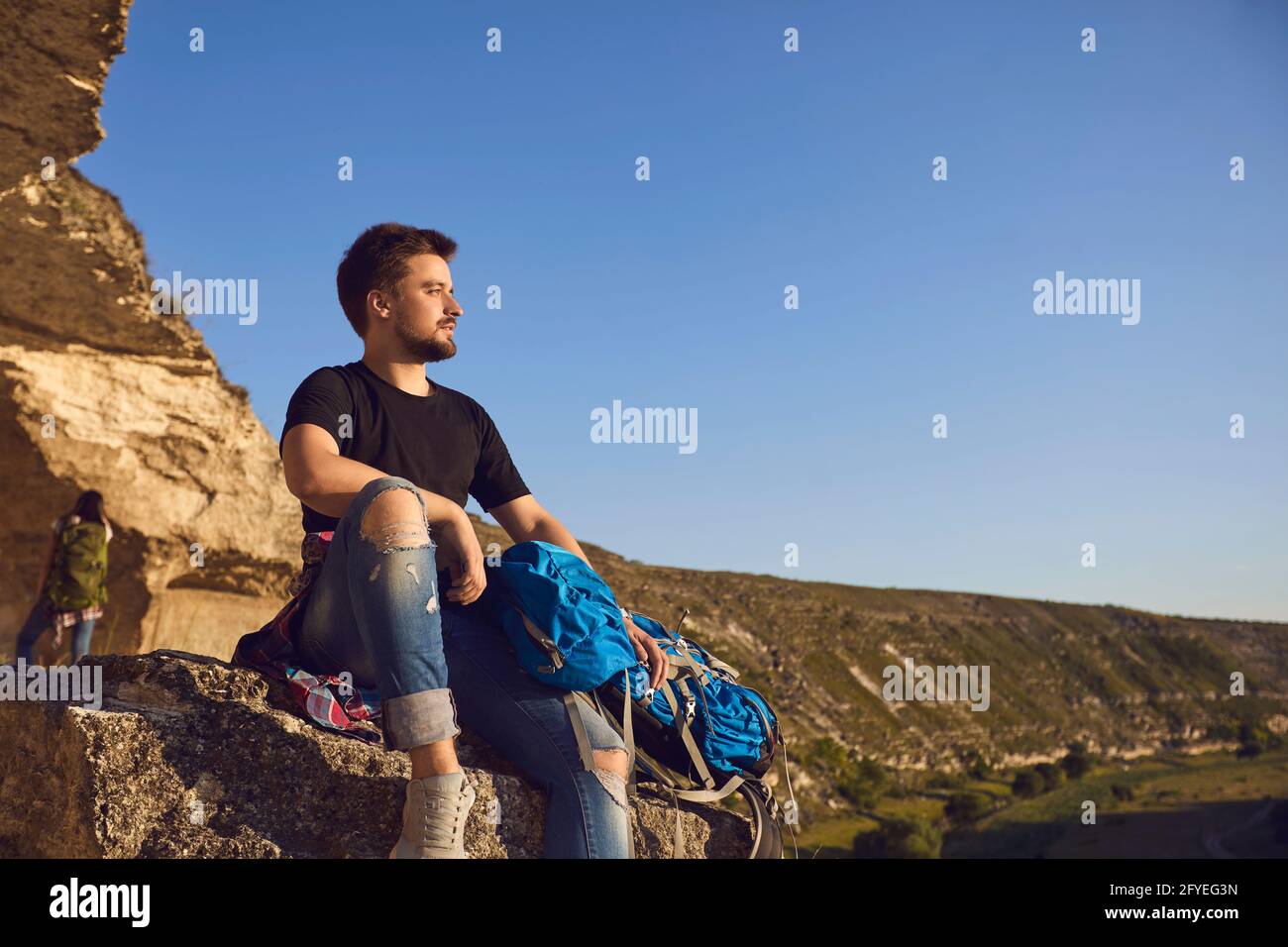 Verträumter junger Wanderer, der am Rande des Berges sitzt und in die Ferne blickt. Stockfoto