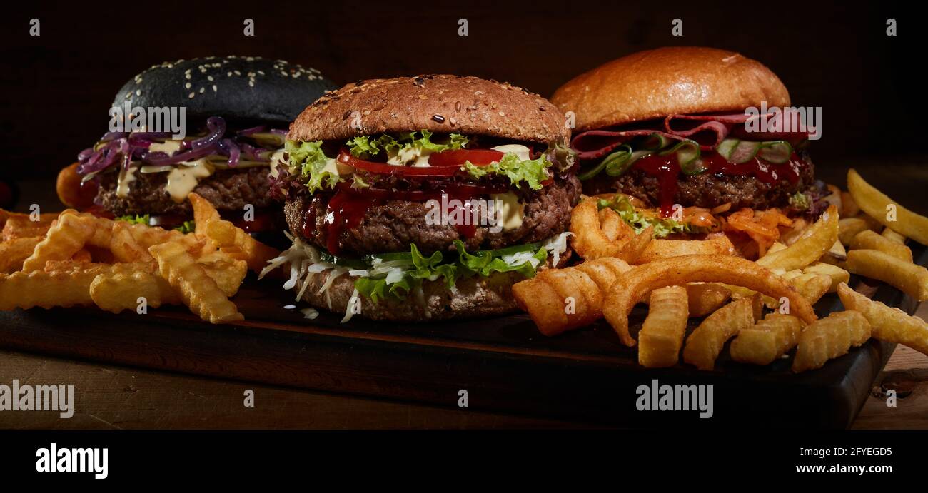 Appetitliche Burger mit verschiedenen Arten von Brötchen auf Holz serviert Brett mit leckeren knusprigen Pommes Stockfoto