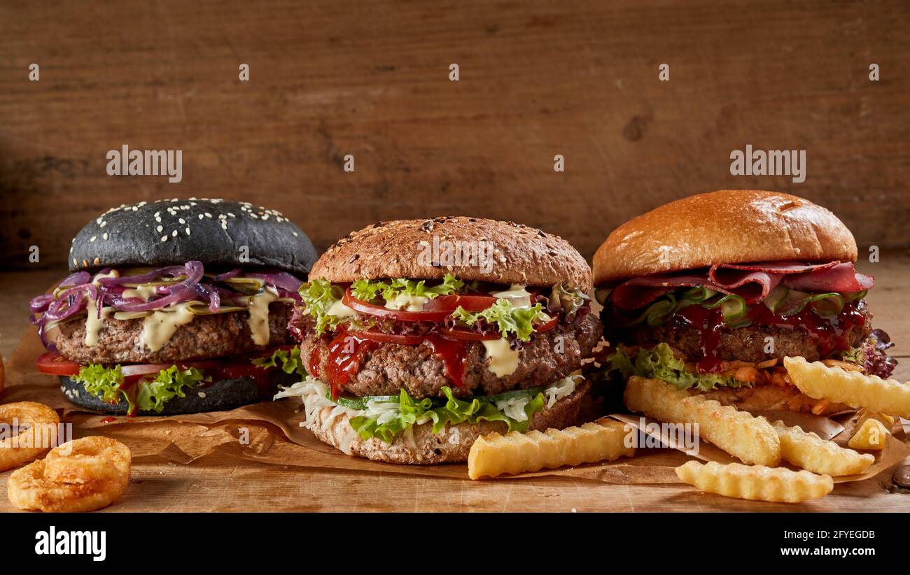Leckere Burger mit verschiedenen Arten von Brötchen auf Holz angeordnet Tisch mit appetitlichen Pommes Stockfoto