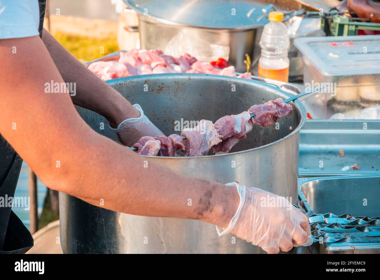 Die Hände eines Mannes, der Fleisch auf einem Grillspieß spieß. Nahaufnahme von rohem Fleisch auf einem Spieß. Street Food Festival. Stockfoto