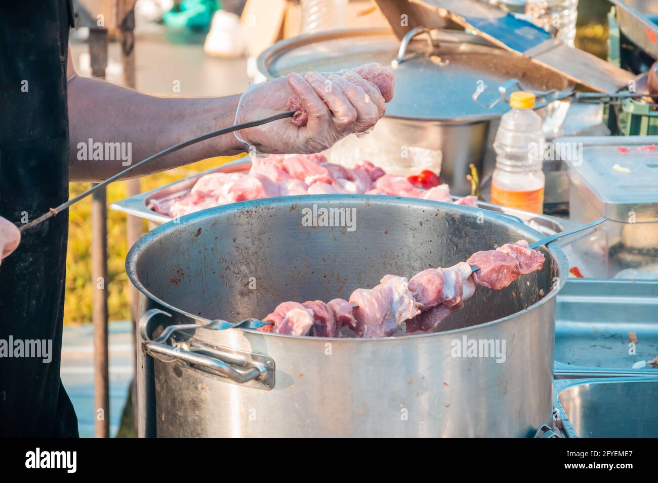 Die Hände eines Mannes, der Fleisch auf einem Grillspieß spieß. Nahaufnahme von rohem Fleisch auf einem Spieß. Street Food Festival. Stockfoto