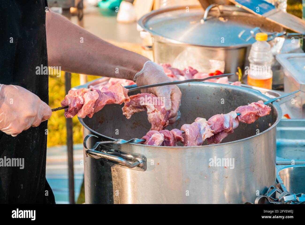 Die Hände eines Mannes, der Fleisch auf einem Grillspieß spieß. Nahaufnahme von rohem Fleisch auf einem Spieß. Street Food Festival. Stockfoto