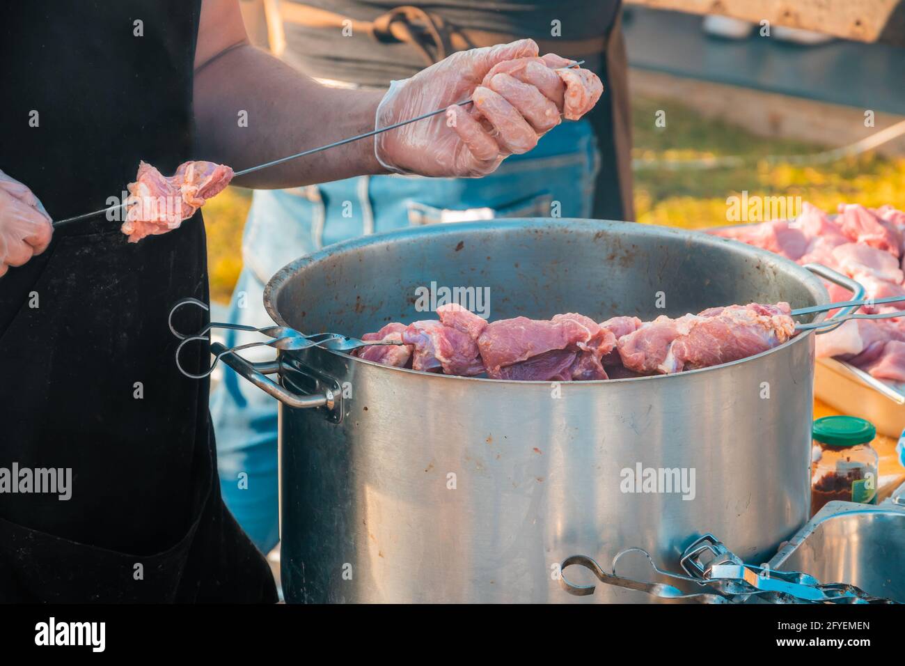 Die Hände eines Mannes, der Fleisch auf einem Grillspieß spieß. Nahaufnahme von rohem Fleisch auf einem Spieß. Street Food Festival. Stockfoto