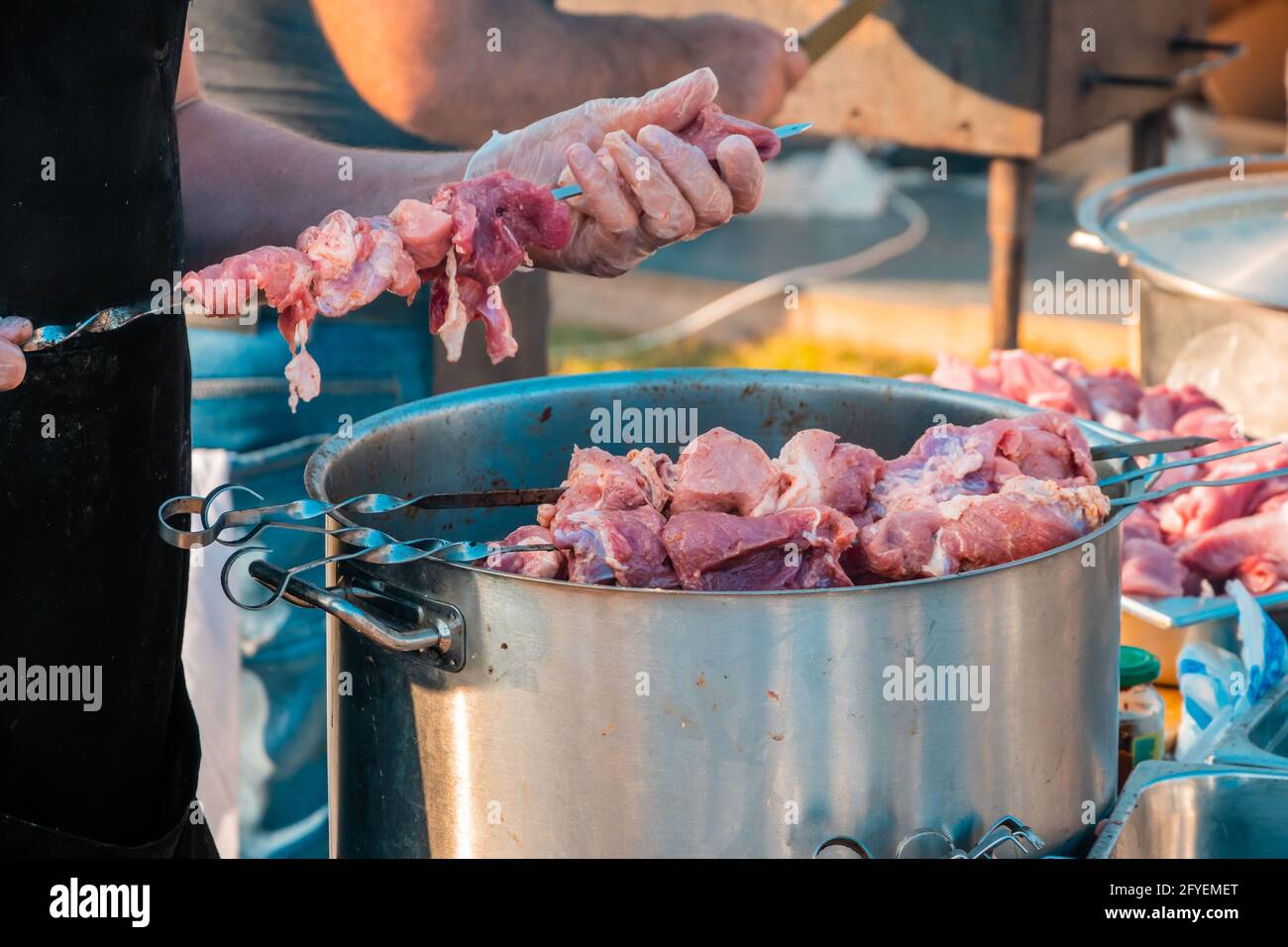 Die Hände eines Mannes, der Fleisch auf einem Grillspieß spieß. Nahaufnahme von rohem Fleisch auf einem Spieß. Street Food Festival. Stockfoto
