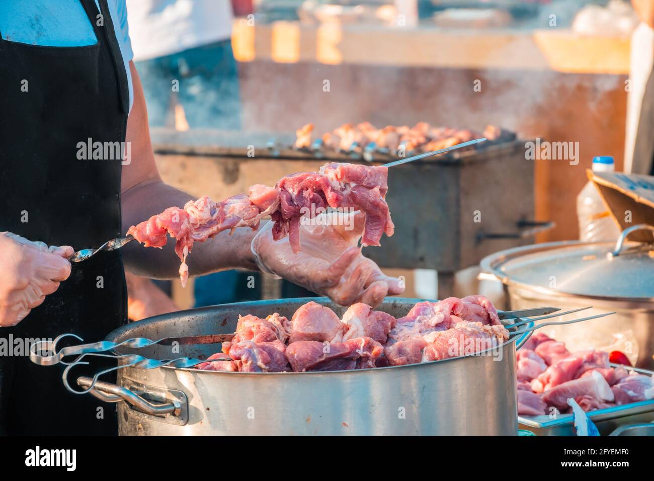 Die Hände eines Mannes, der Fleisch auf einem Grillspieß spieß. Nahaufnahme von rohem Fleisch auf einem Spieß. Street Food Festival. Stockfoto