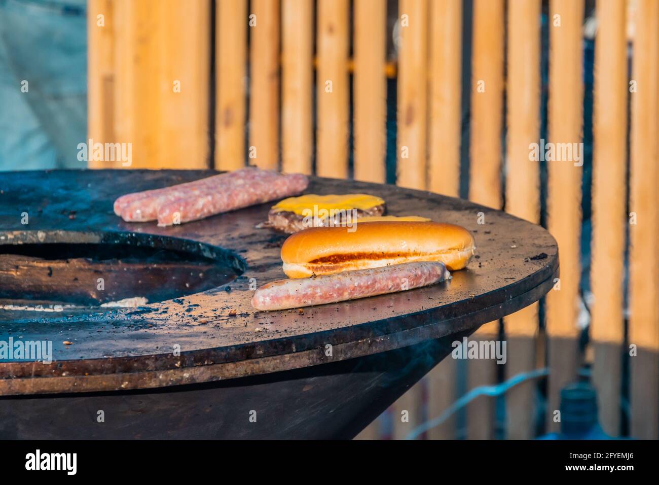 Gegrillte Würstchen, Steaks und Brotscheiben auf einem großen Grill im Freien. Grillfest im Stadtpark. Stockfoto