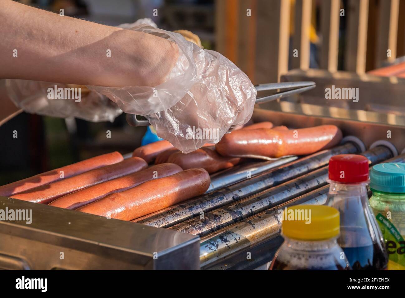 Der Koch nimmt eine auf einem rotierenden Schweißgerät gebratene Wurst. Grillfest im Stadtpark. Street Fast Food. Stockfoto