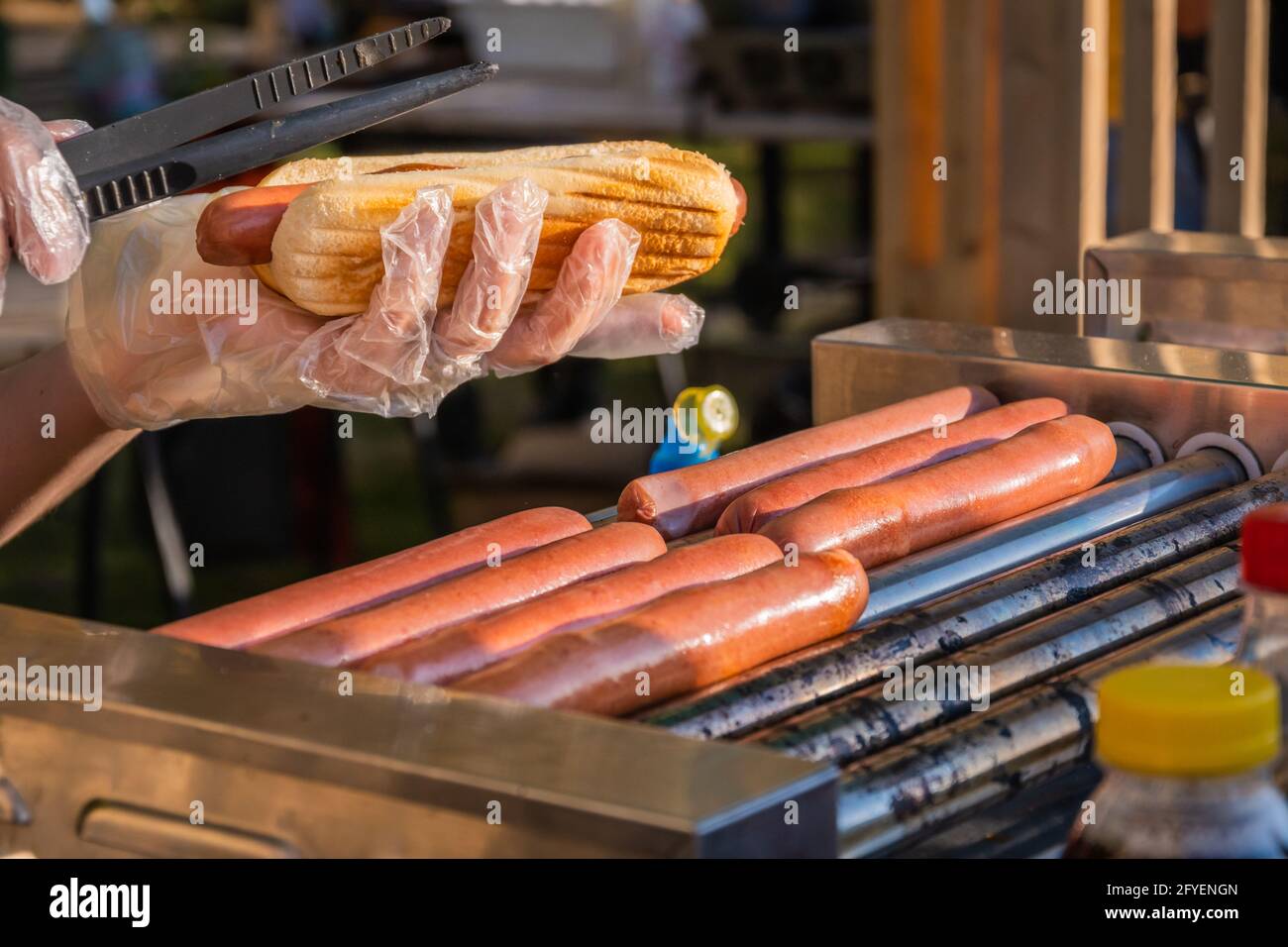 Frischer Hot Dog mit gebratener Wurst, serviert in einem Café im Freien. Kochen amerikanischer Grillgerichte. Grillfest im Stadtpark. Street Fast Food. Stockfoto