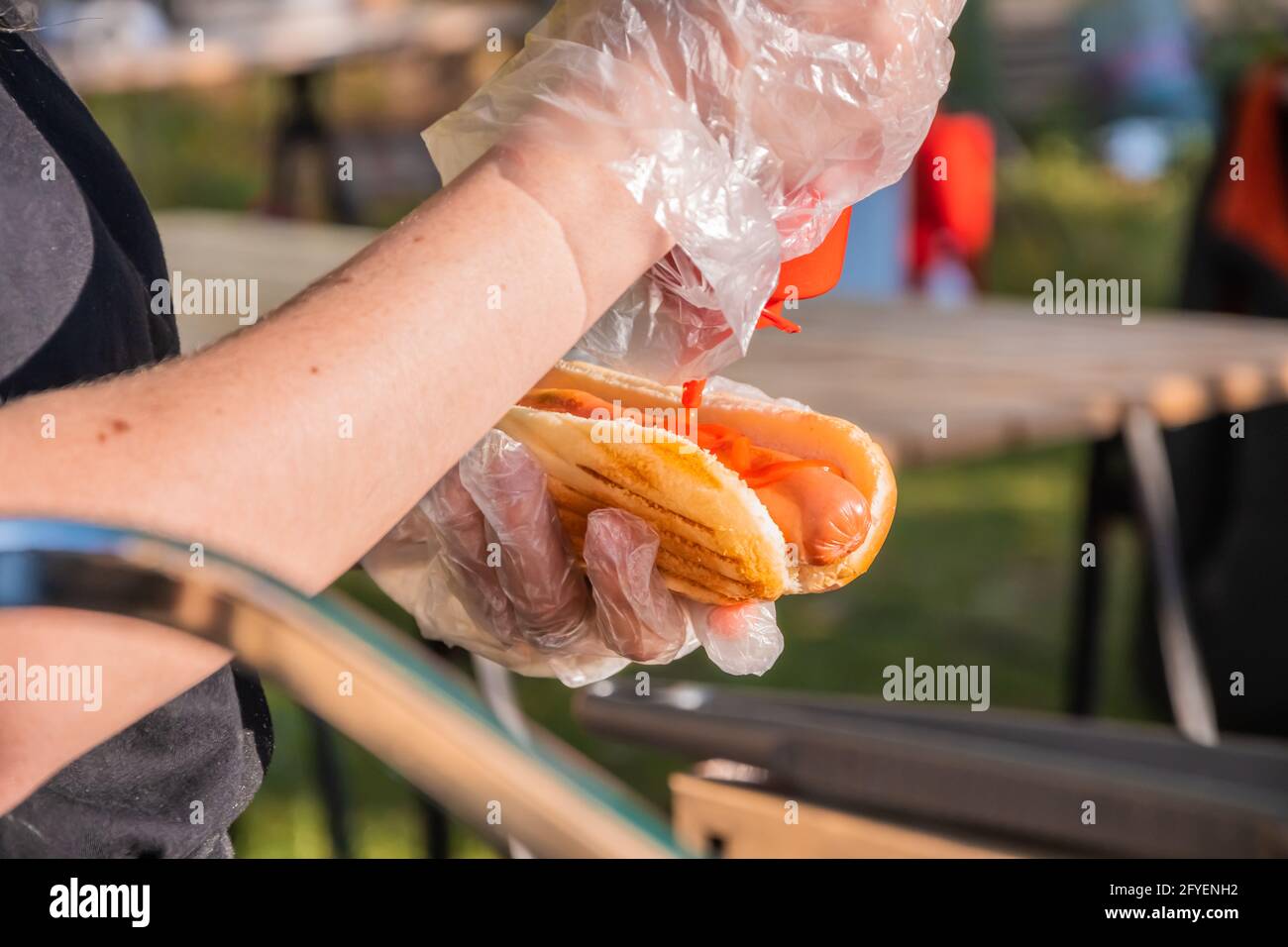 Frischer Hot Dog mit gebratener Wurst, serviert in einem Café im Freien. Kochen amerikanischer Grillgerichte. Der Koch füllt einen Hot Dog mit Ketchup. Grillfest Stockfoto