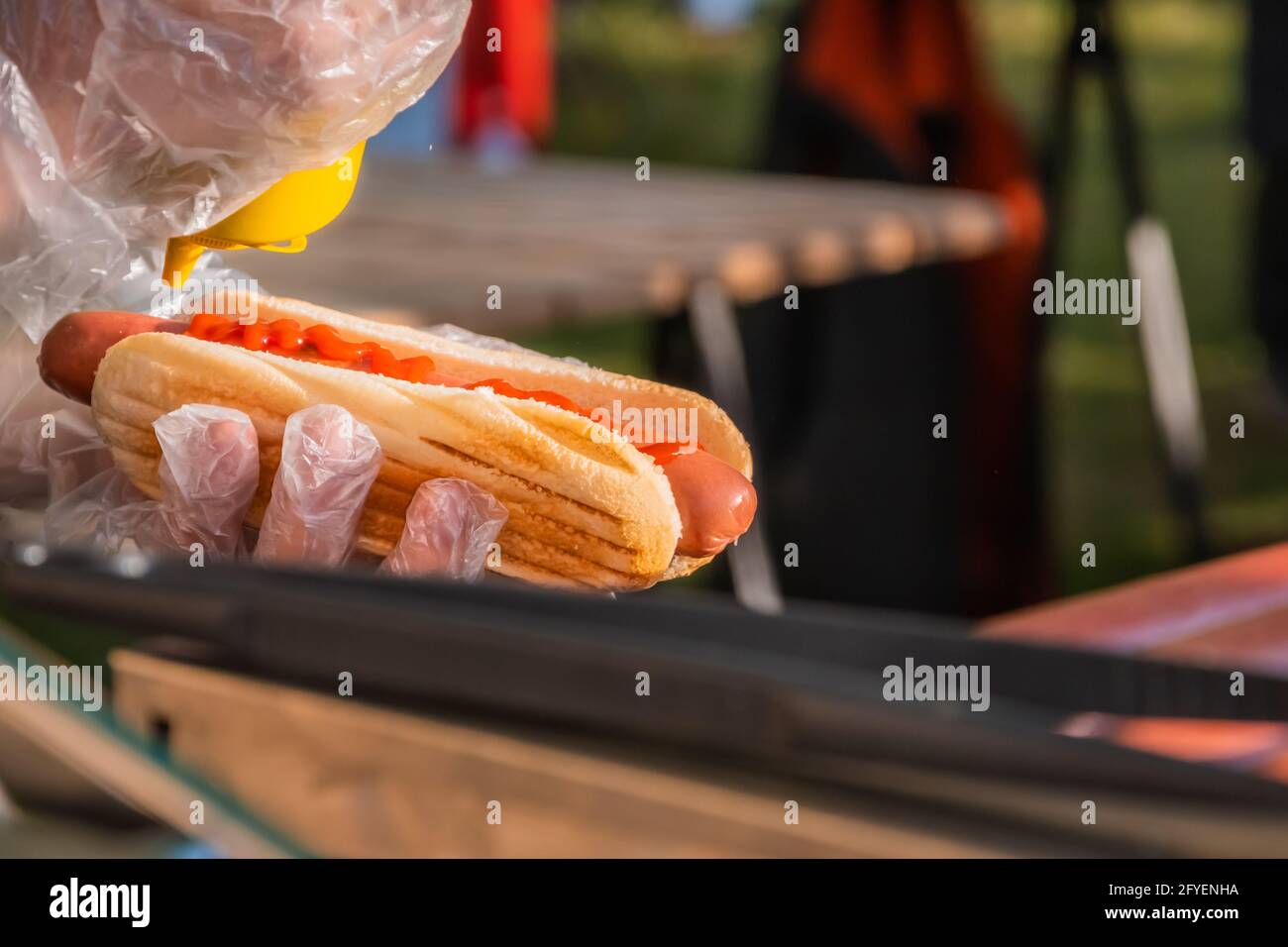 Frischer Hot Dog mit gebratener Wurst, serviert in einem Café im Freien. Kochen amerikanischer Grillgerichte. Der Koch füllt einen Hot Dog mit Senf. Grillfest Stockfoto